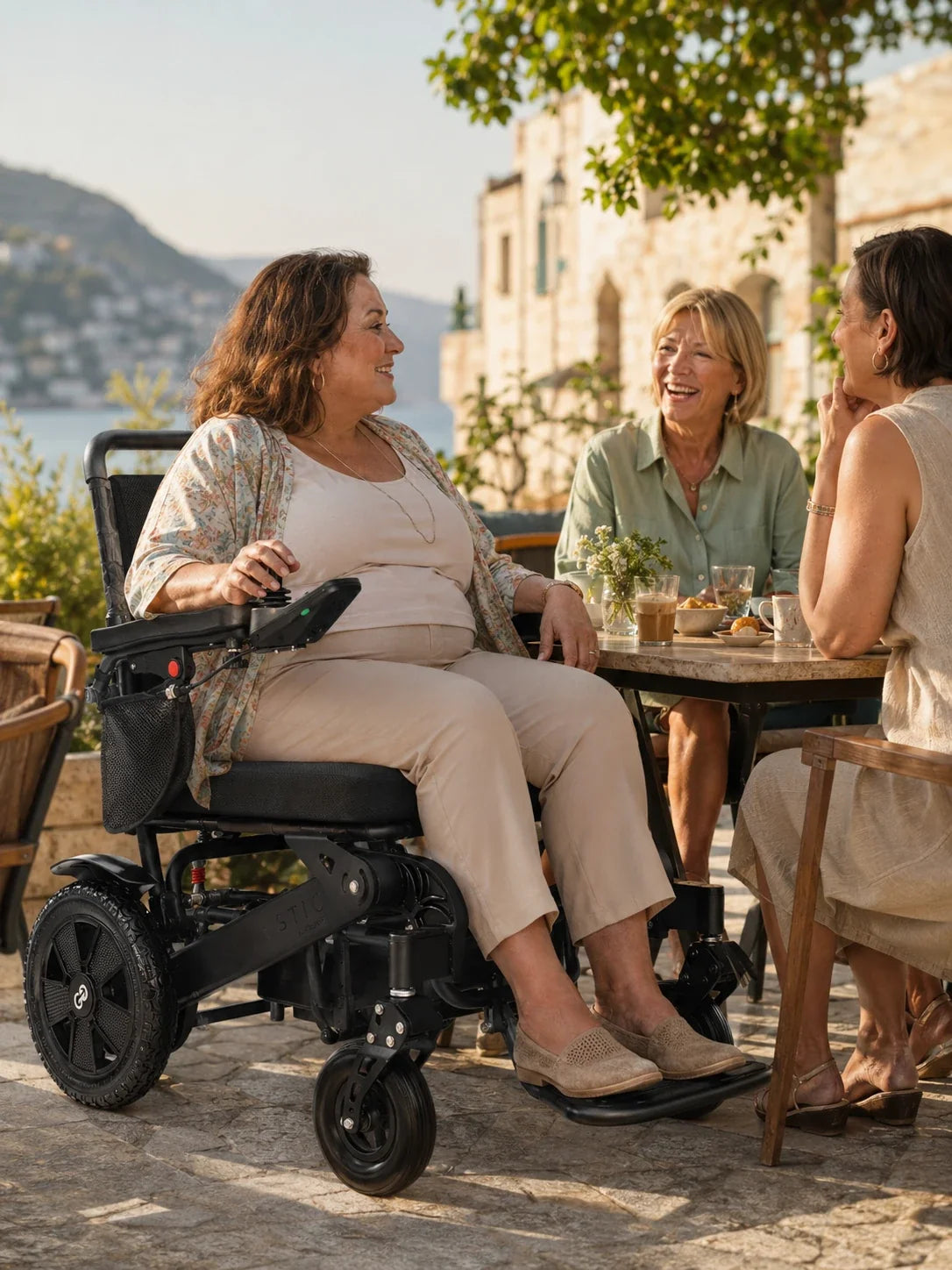 Electric wheelchair ComfyGO Majestic 440 HD Plus – woman seated in chair, talking with two friends at outdoor cafe