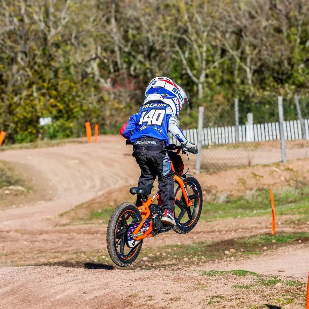 Electric Bike Apollo Sedna 16 Rxf is an orange electric bike being jumped by a rider on a dirt track.
