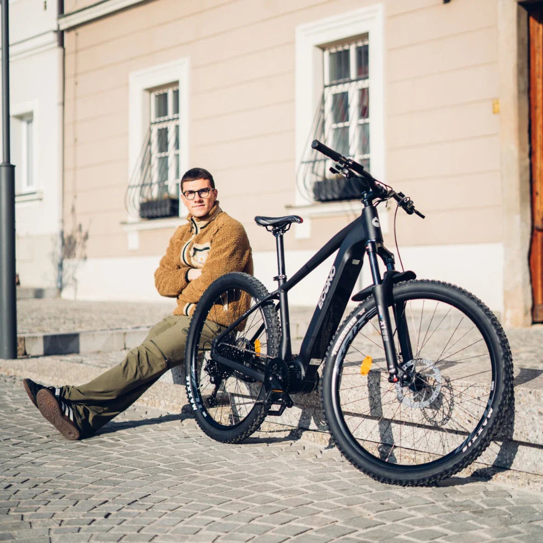 A person sitting on steps next to an electric bike Econo Gams SUV C6 in a sunny urban setting