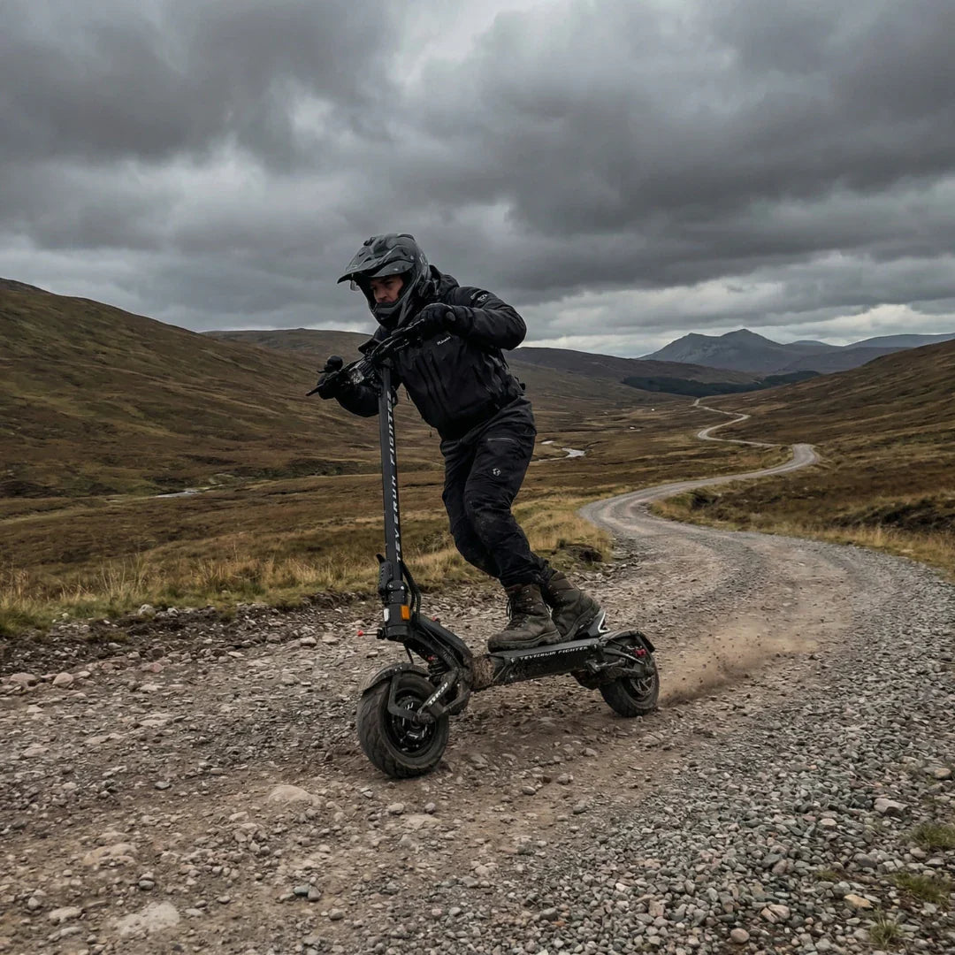 Electric scooter Teverun Fighter 11+ 2026 – rider on winding gravel road, cloudy sky