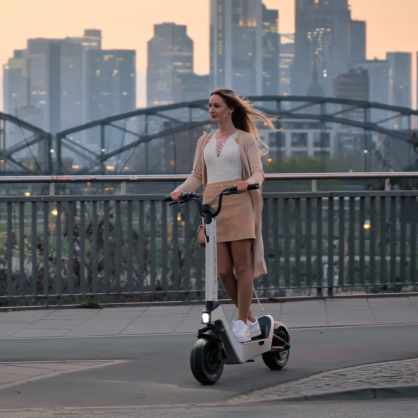 Električni romobil StreetBooster Pollux – žena vozi po mostu, grad u pozadini