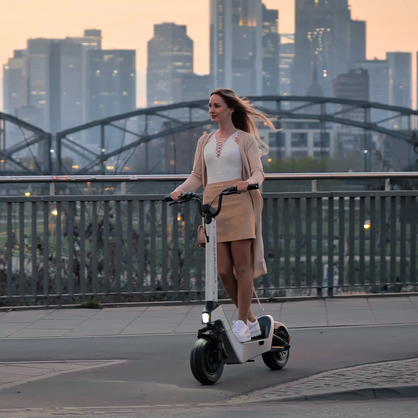 Električni romobil StreetBooster Pollux – žena vozi po mostu, grad u pozadini