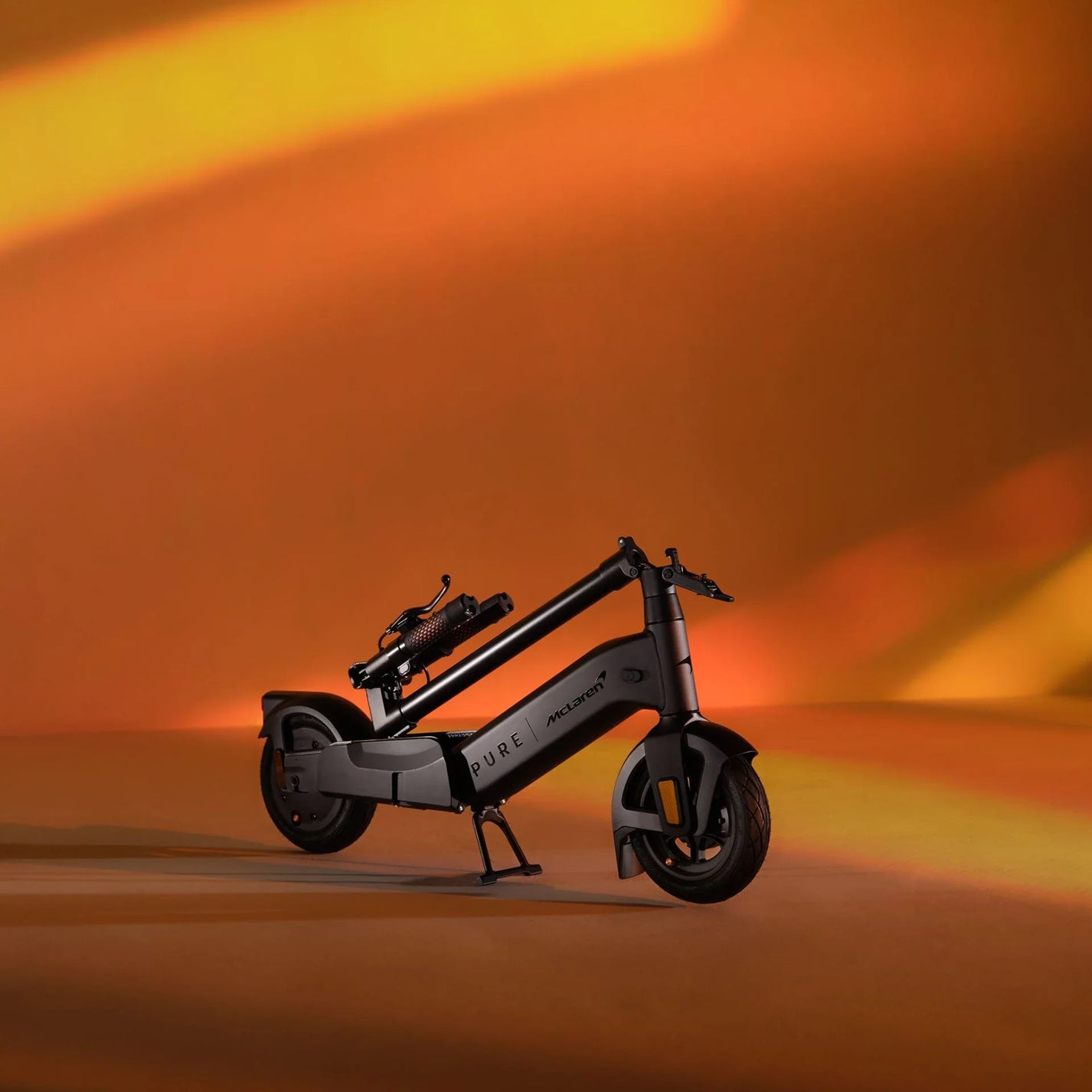 Electric scooter Pure Advance+ McLaren Edition – folded, against orange background