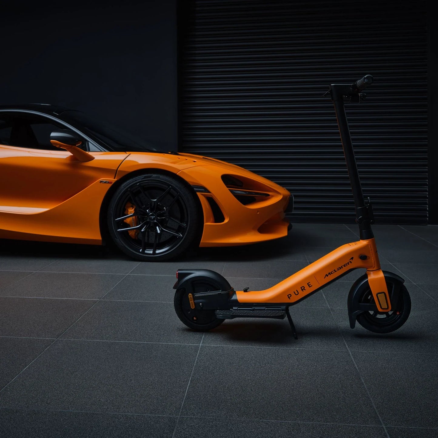 Electric scooter Pure Advance+ McLaren Edition – orange colour variant next to sports car