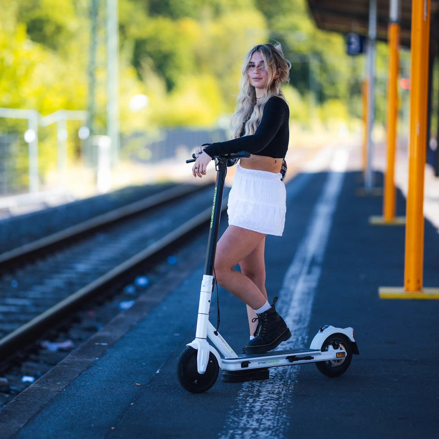 Električni romobil StreetBooster Vega – žena s bijelim romobilom na željezničkoj platformi