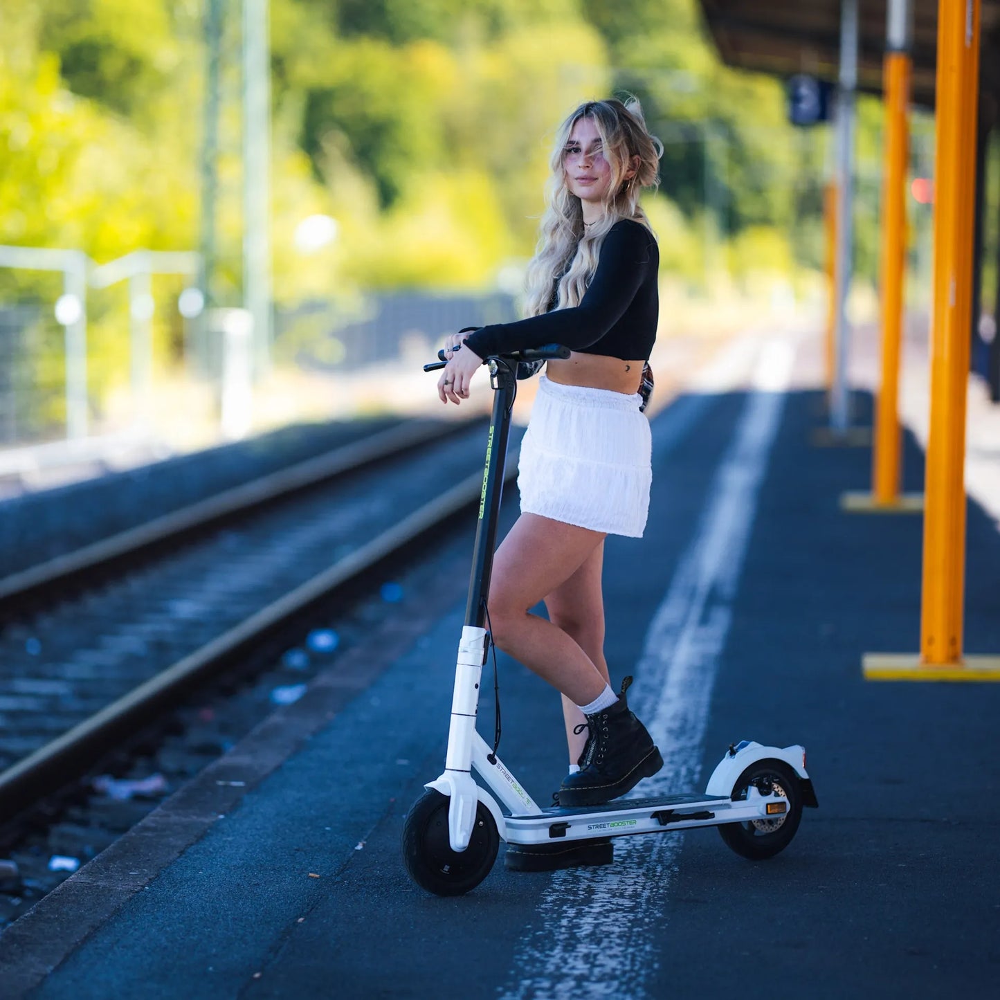 Električni romobil StreetBooster Vega – žena s bijelim romobilom na željezničkoj platformi