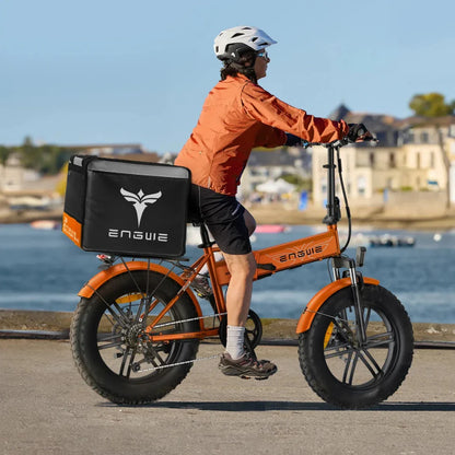 A person rides an orange electric bike Engwe EP 2 Boost with a delivery bag in a scenic outdoor setting