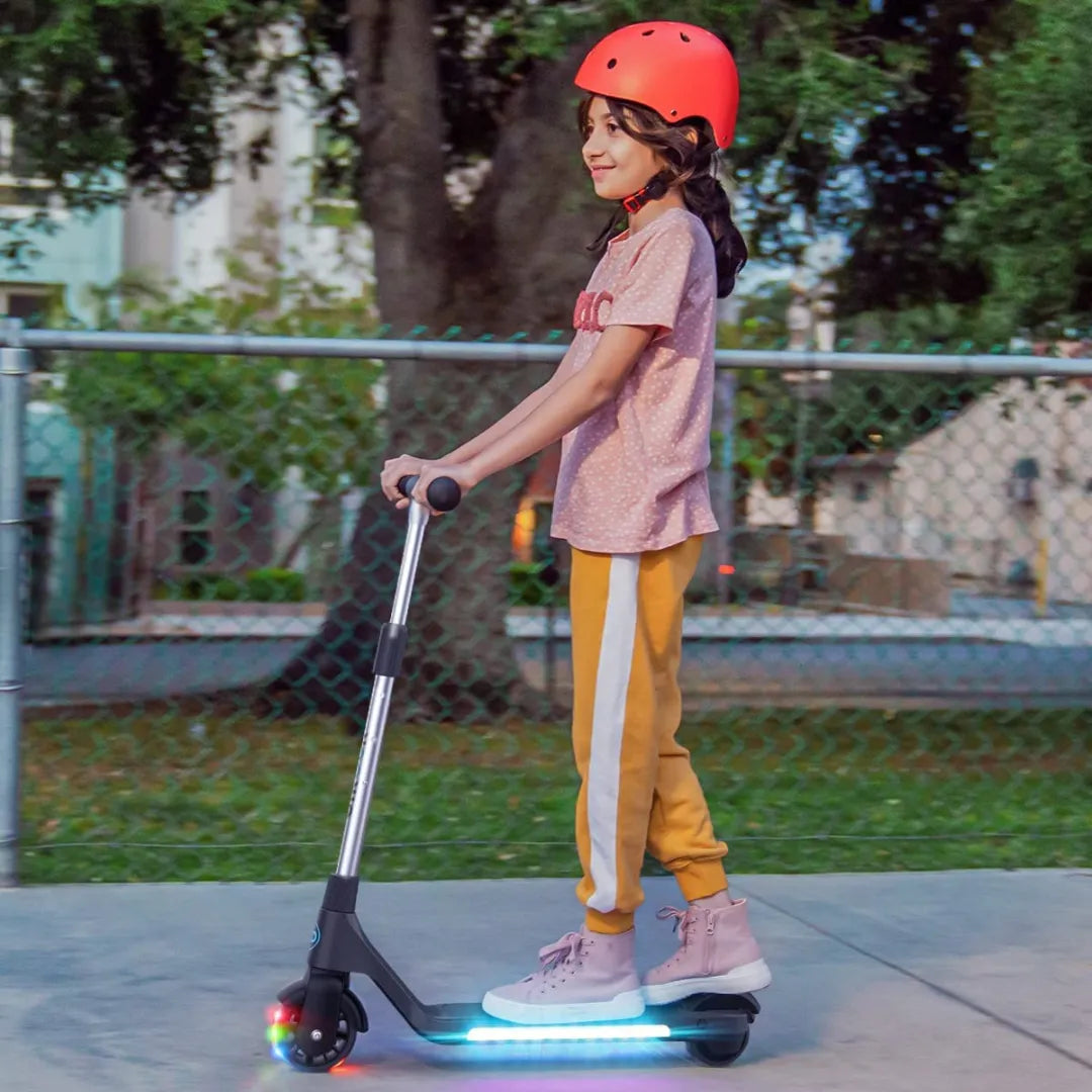 The child is riding a Gyroor H30 electric scooter, wearing a red helmet and wearing normal clothes