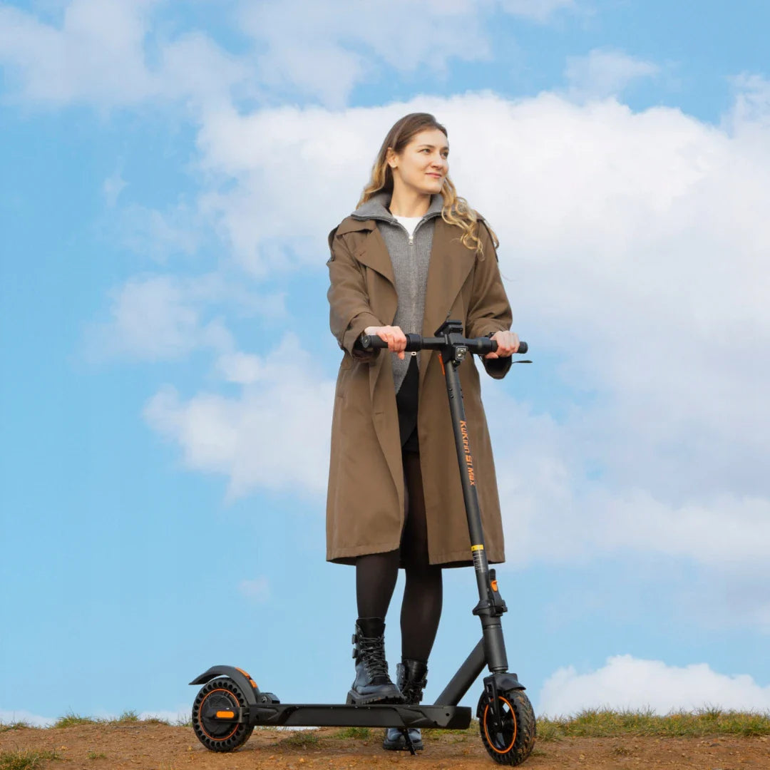 A woman is standing on a Kukirin S1 Max electric scooter in the middle of a blue sky with clouds