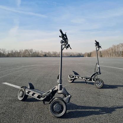 Two electric scooters, the Nami Blast 2 Max, are parked on a smooth asphalt surface under a clear blue sky