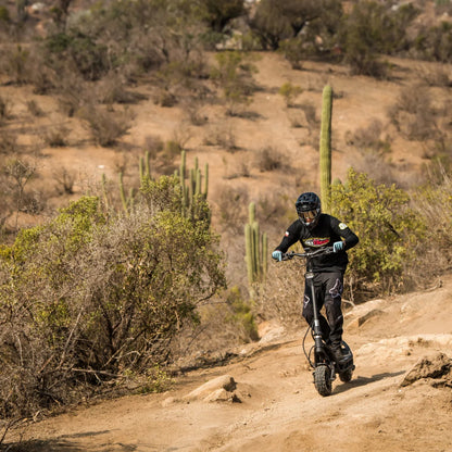 Electric Scooter Nami Burn E 3 Max, rugged design, man riding on rough terrain, surrounded by a desert landscape.