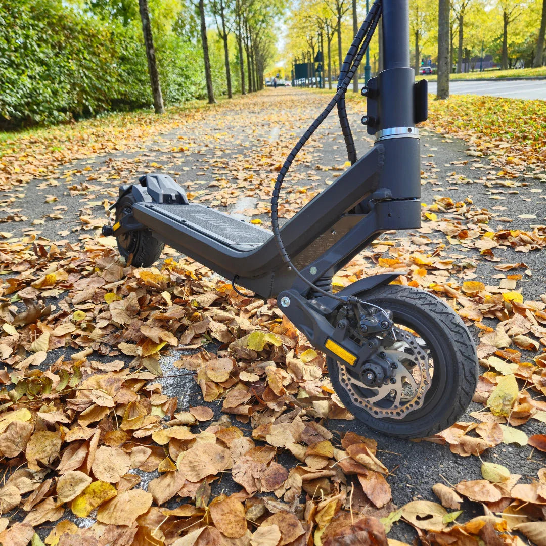 Electric Scooter Nami Stellar features a sleek design resting on a bed of autumn leaves, showcasing its robust wheels and build.