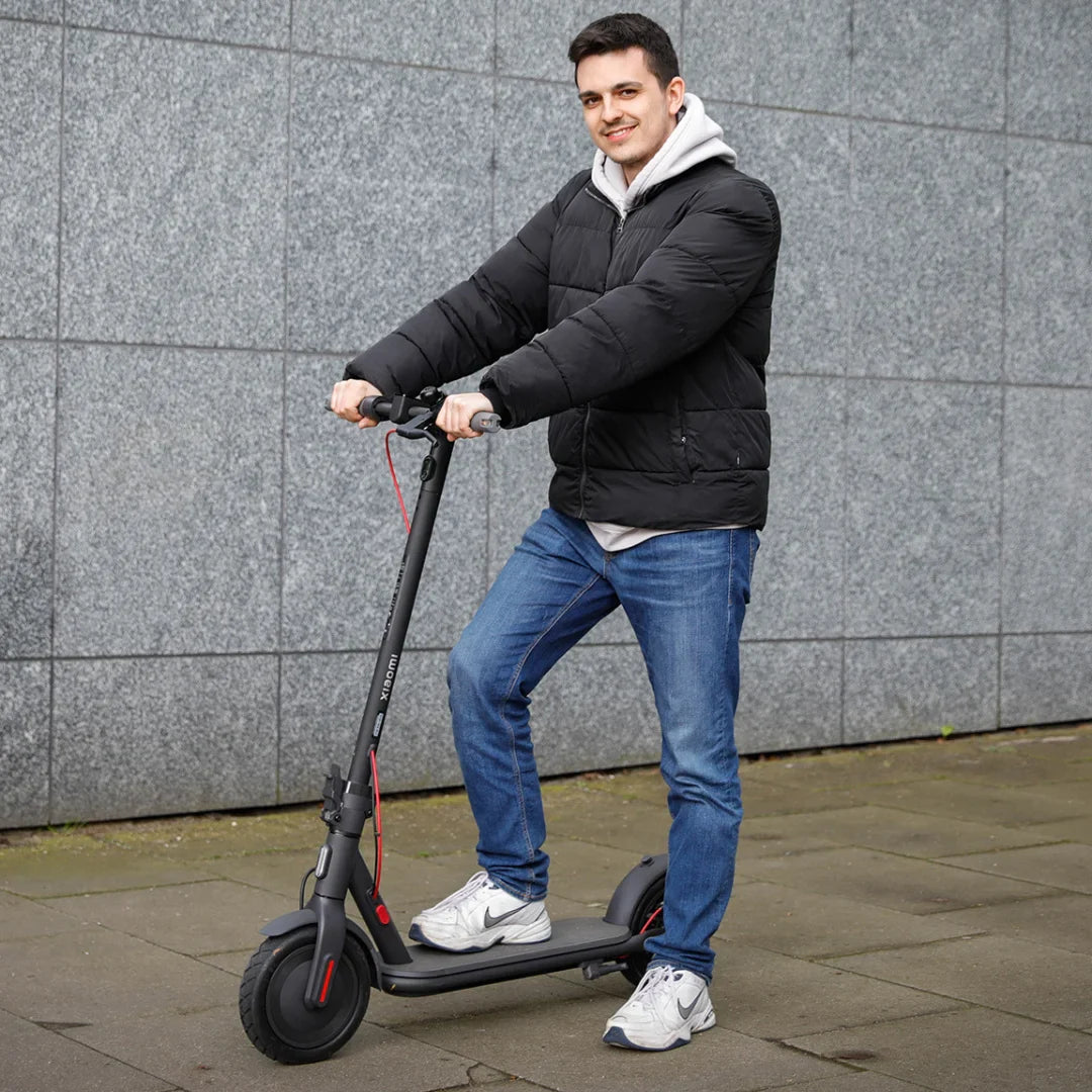 Electric Scooter Xiaomi 4 Eu, sleek black design, young man riding, urban setting, perfect for commuting.